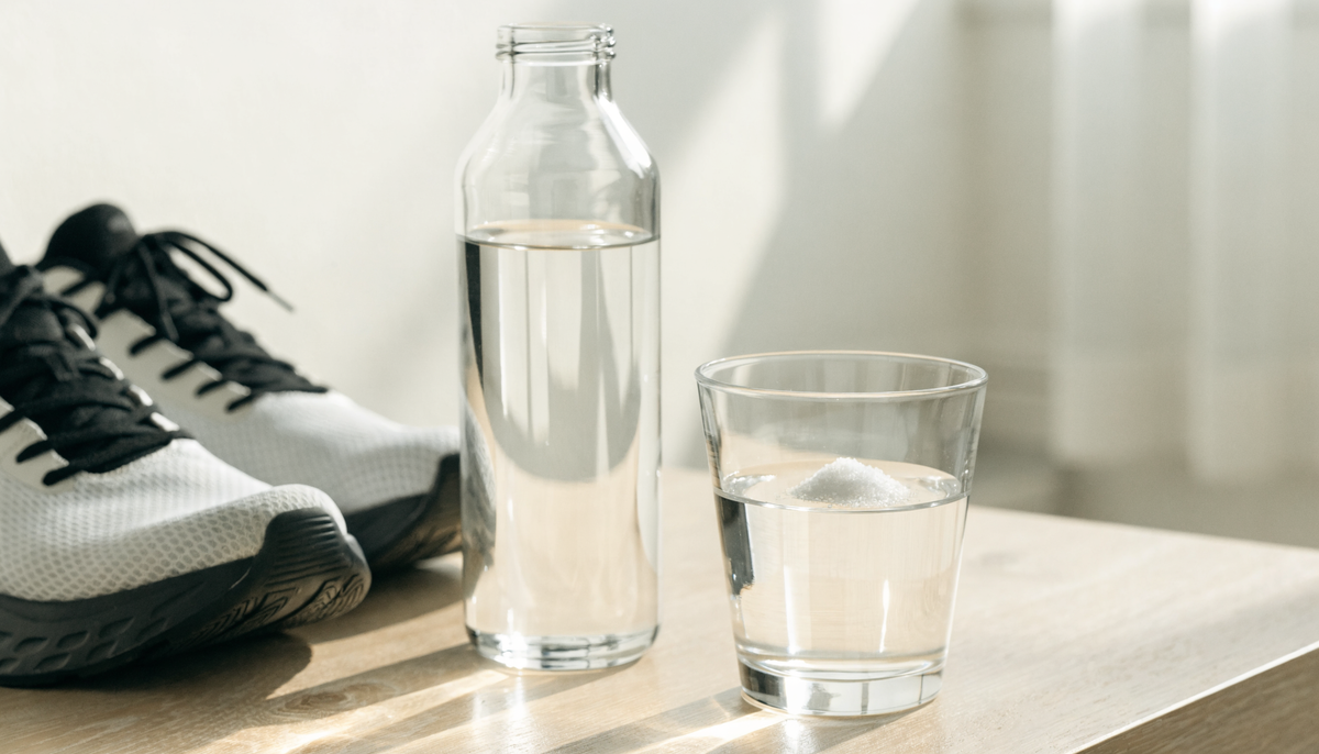 Bouteille d'eau et verre avec une pincée de sel de mer à côté de chaussures de running